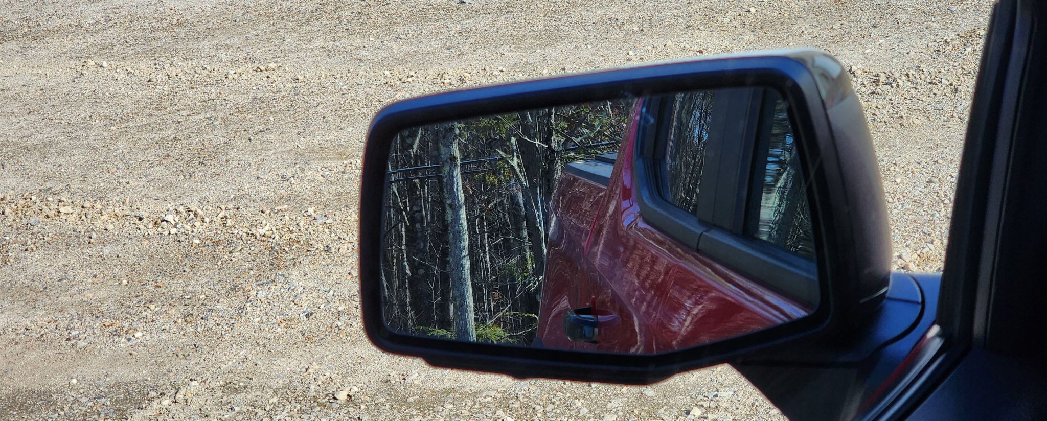 A driver's rear view mirror of a red Chevrolet Silverado