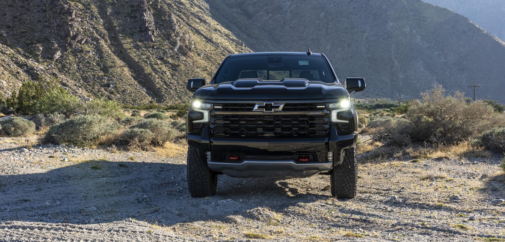 A straight on view of a 2024 Chevrolet Silverado in a desert environment with a mountain behind it.