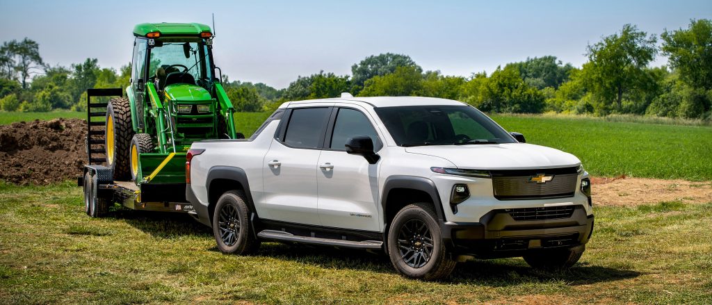 Front 3/4 view of the Silverado EV WT towing a trailer with a farming tractor.