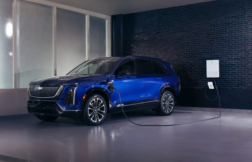 Blue 2026 Cadillac Vistiq EV charging in a garage with a wall-mounted home charger.