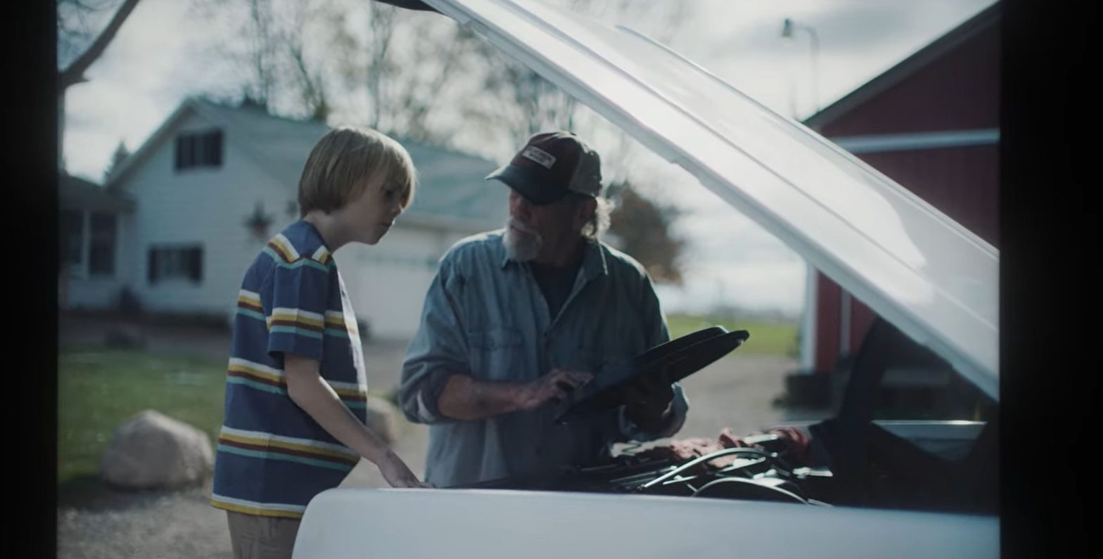 A grandfather and grandson working together under the hood of a classic white Chevrolet truck, sharing a heartfelt moment.