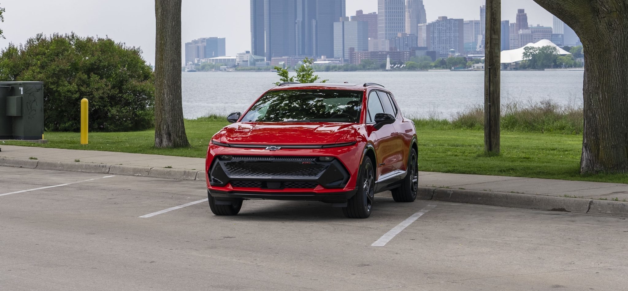 Red Chevrolet Equinox EV parked near Detroit skyline, symbolizing the controversy over its infotainment subscription model.